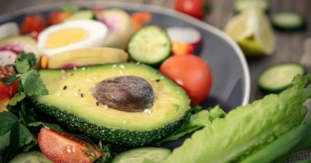 Dieta cetogênica. Prato com abacate cortado ao meio, ovo cozido, tomate, pepino e folhas verdes, representando uma refeição low carb.