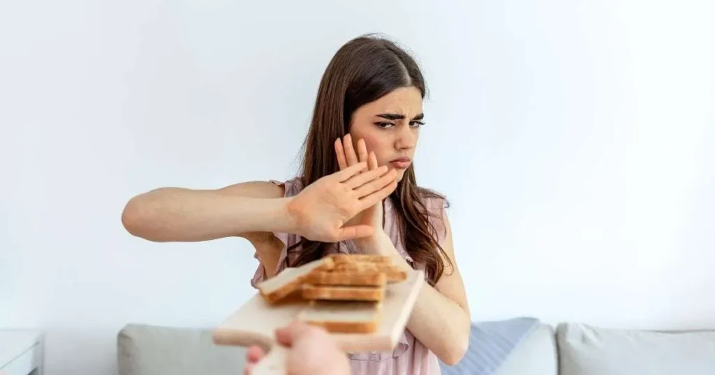 Jovem recusando fatias de pão com expressão de desagrado, gesticulando com a mão em sinal de negação.