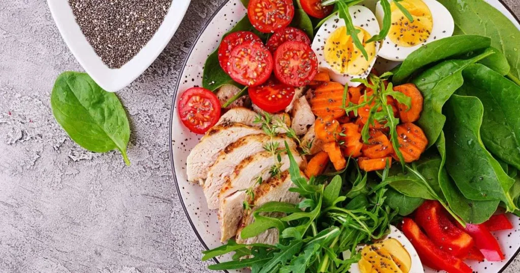 Prato colorido com peito de frango grelhado, ovos cozidos, tomates cereja, cenoura e folhas verdes, representando uma refeição equilibrada permitida na dieta para SIBO.