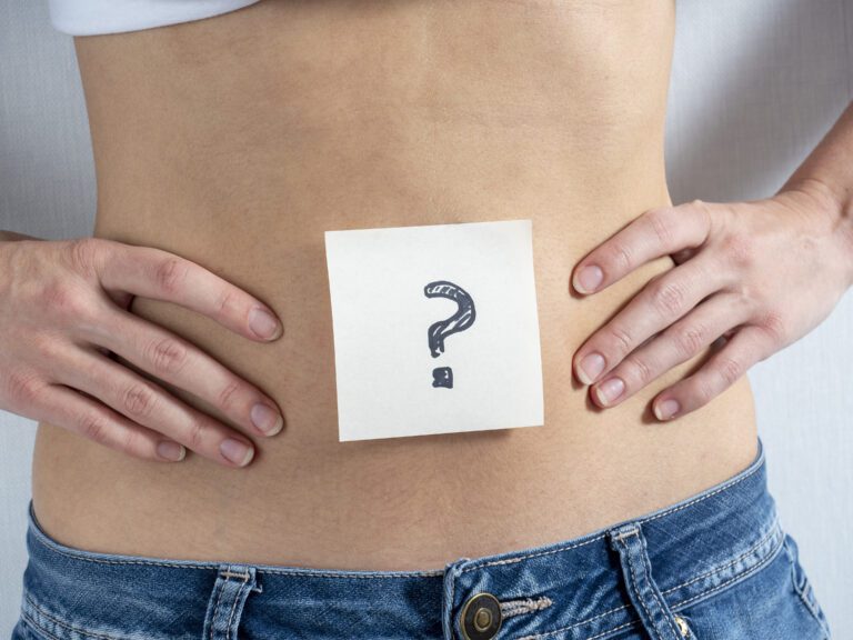 the woman points with her hands at a paper sticker with a question mark taped to her bare stomach. The concept of pregnancy and gender uncertainty
