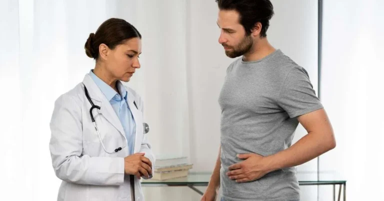 Homem com a mão no abdômen expressando desconforto durante consulta com médica, representando a investigação clínica das causas do SIBO e problemas digestivos.