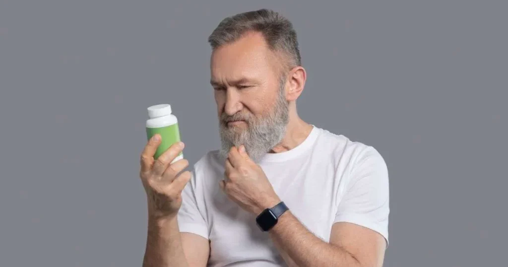 Suplementação de ferro. Homem mais velho analisando o rótulo de um suplemento em frasco verde com expressão pensativa.