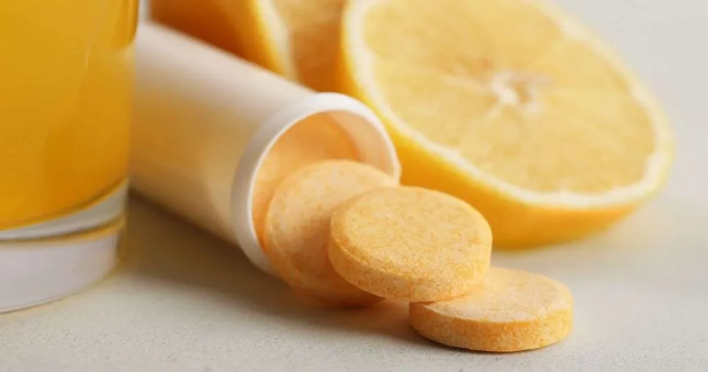 Comprimidos efervescentes de vitamina C saindo do frasco ao lado de laranja cortada e copo com suco