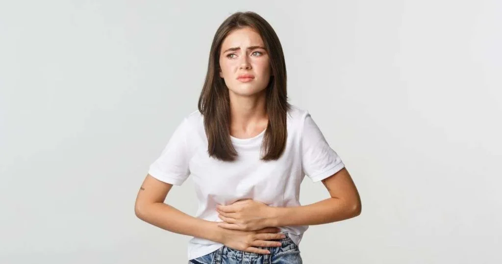 Mulher jovem com expressão de desconforto segurando o abdômen, representando sintomas da síndrome do intestino irritável.