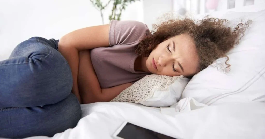 SII pós-COVID-19: Mulher deitada na cama com expressão de desconforto segurando o abdômen, representando sintomas da síndrome do intestino irritável após a COVID-19.