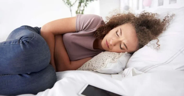 SII pós-COVID-19: Mulher deitada na cama com expressão de desconforto segurando o abdômen, representando sintomas da síndrome do intestino irritável após a COVID-19.