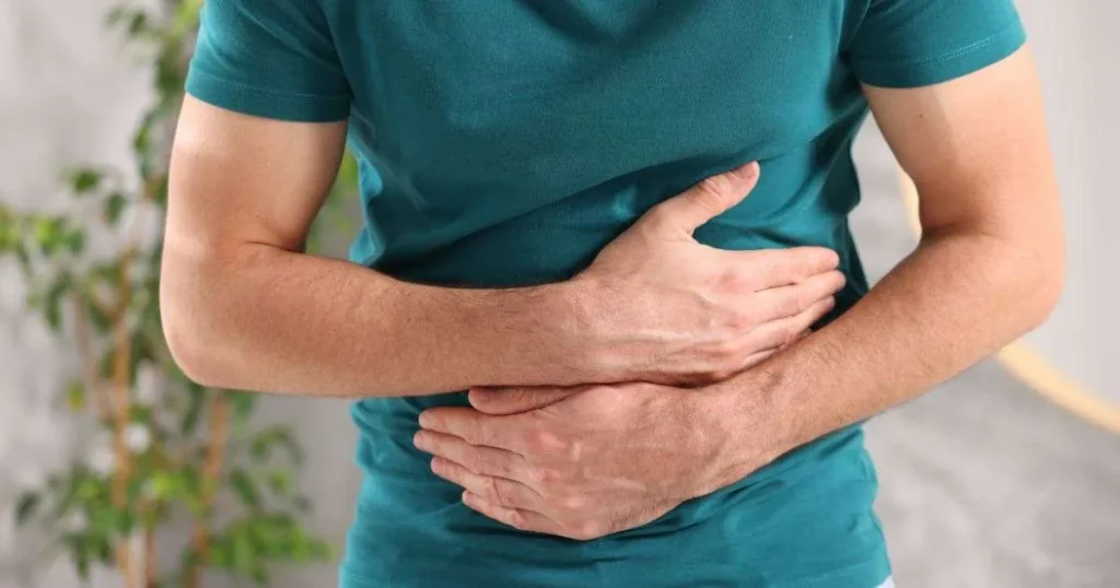 Homem segurando o abdômen com as duas mãos em gesto de dor ou desconforto na região intestinal