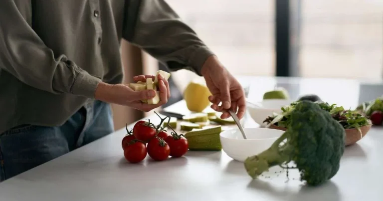 Pessoa preparando refeição com legumes frescos na bancada da cozinha, incluindo tomate cereja, brócolis e abobrinha