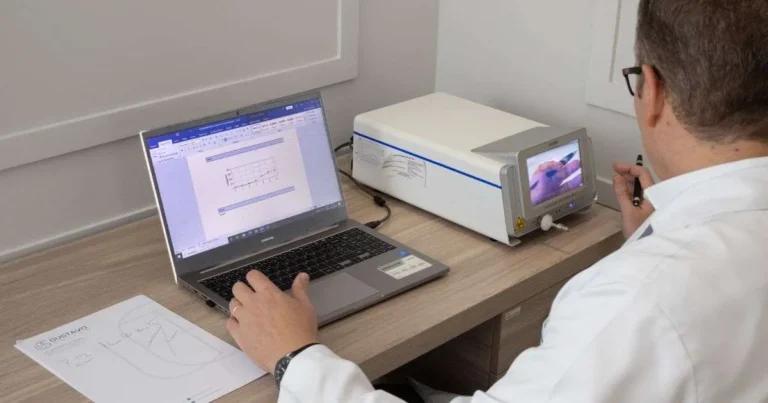 Médico de jaleco branco analisando resultados no notebook ao lado de aparelho de teste respiratório em consultório